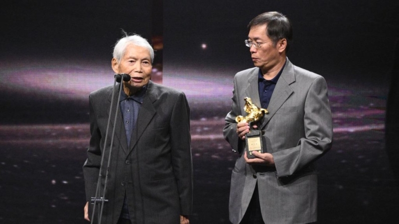 攝影師林文錦（右）獲金馬獎頒終身成就獎，由兒子攙扶上臺領獎。