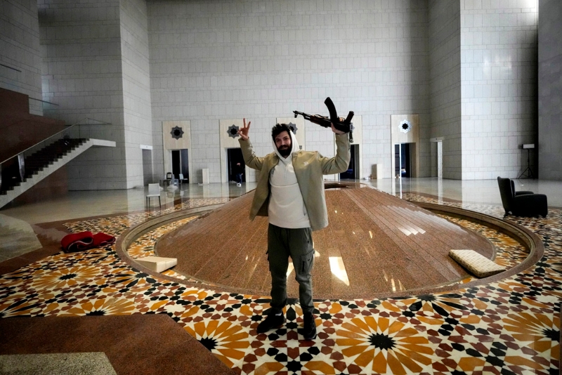 敘利亞總統巴沙爾·阿薩德（Bashar al-Assad）搭機逃亡后，敘利亞叛軍及民眾闖進總統府洗劫，還發現阿塞德有一整排賓士、法拉利、保時捷等豪車收藏。圖為8日一名男子手持AK-47在總統府拍照。