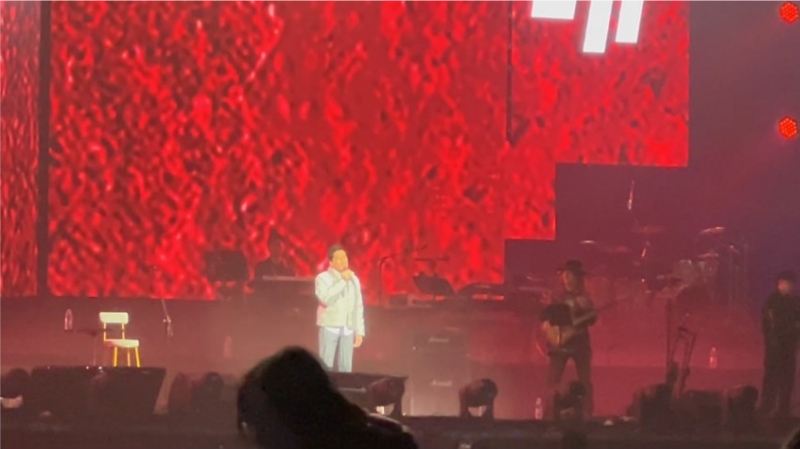 齊秦身穿白色襯衫及銀色羽絨服，下身則穿著黑白條紋長褲配運動波鞋，整體造型十分隨性休閑。